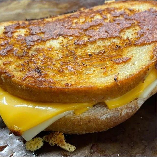 Close-up of a grilled cheese sandwich from a mobile kitchen, with melted cheese between two toasted slices of bread.