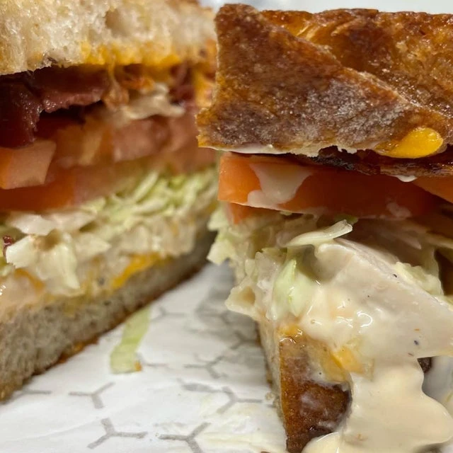 Close-up of a sandwich from a mobile kitchen with crispy bread, layered with tomatoes, lettuce, and a creamy sauce, on a paper towel.