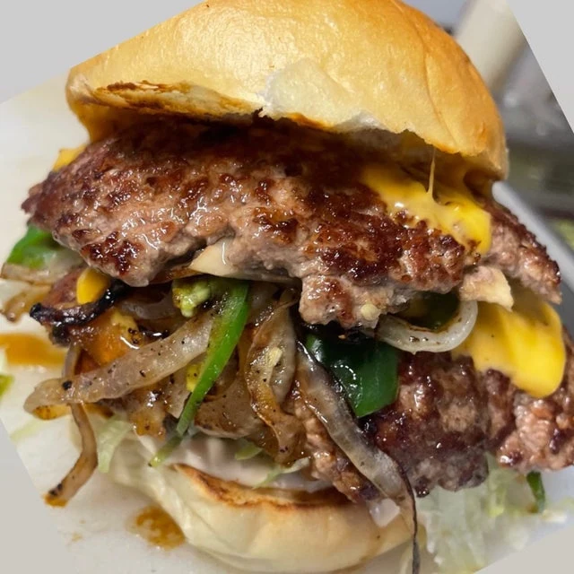 A smashburger with a beef patty, sautéed onions and peppers, lettuce, and sauce on a toasted bun.