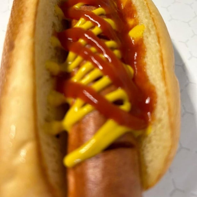 Close-up of a hot dog with mustard and ketchup in a bun, served from a mobile kitchen.