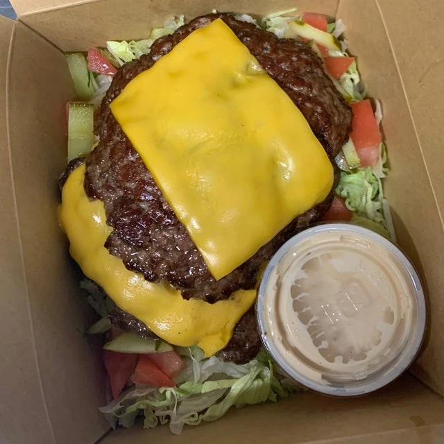 Double cheeseburger with lettuce and tomato from a mobile kitchen, served in a takeout box, accompanied by a side of sauce.