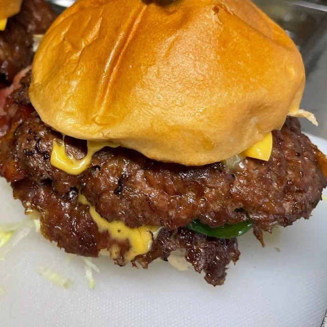 Close-up of a juicy double cheeseburger from a mobile kitchen with melted cheese and fresh toppings on a shiny brioche bun.