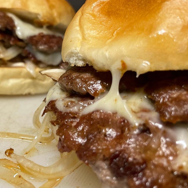 Close-up of a cheeseburger with melted cheese and grilled onions on a toasted bun, prepared in a mobile kitchen.