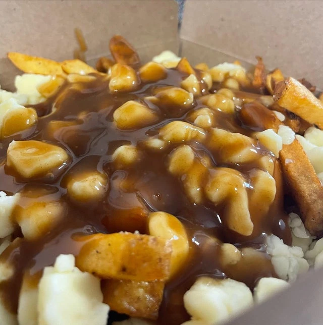 A close-up of poutine prepared in a mobile kitchen, featuring fries, cheese curds, and brown gravy in a cardboard container.