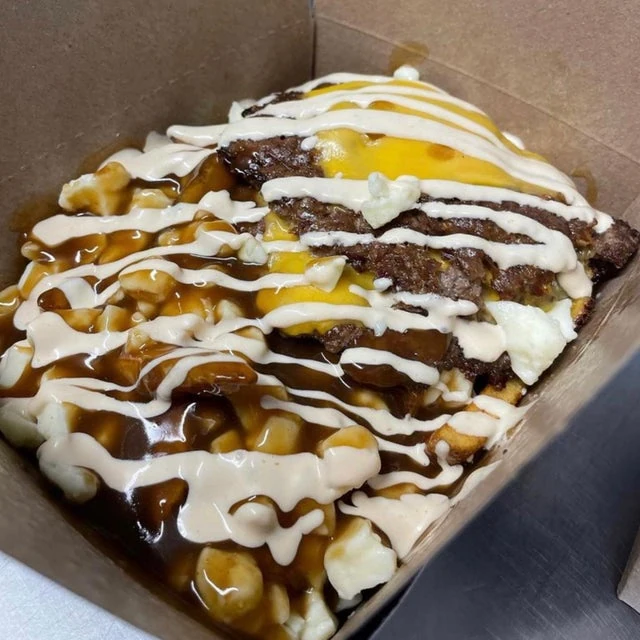 A mobile kitchen serving a cardboard box containing poutine topped with hamburger patties, cheese, gravy, and drizzled sauces.