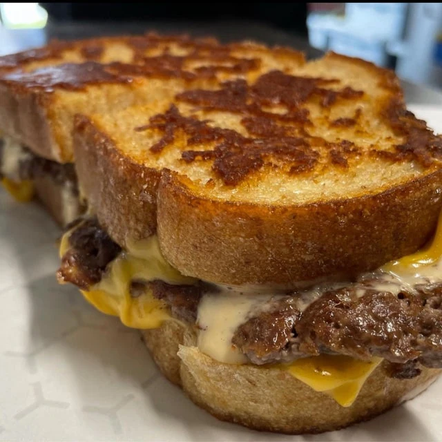 Grilled cheese sandwich with melted cheese and beef patties from a mobile kitchen on a white plate.
