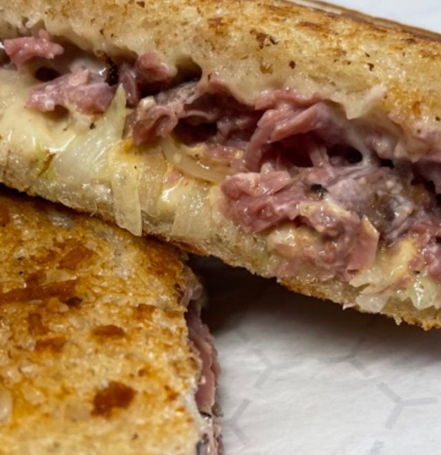 Close-up of a toasted sandwich cut in half, prepared in a mobile kitchen, filled with melted cheese and shredded meat on a white plate.