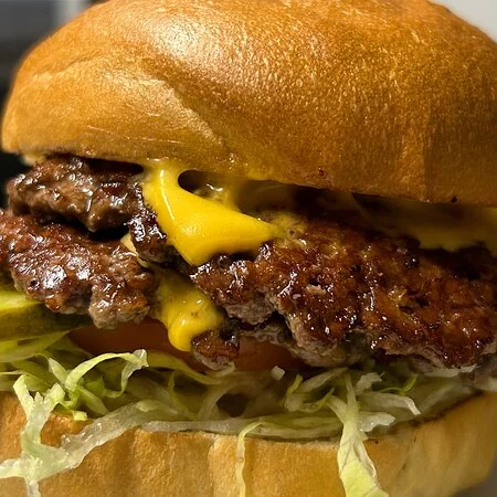 Close-up view of a cheeseburger with melted cheese, shredded lettuce, and a grilled beef patty in a toasted bun prepared in Pearson Street Smashburgers N’ Melts mobile kitchen,